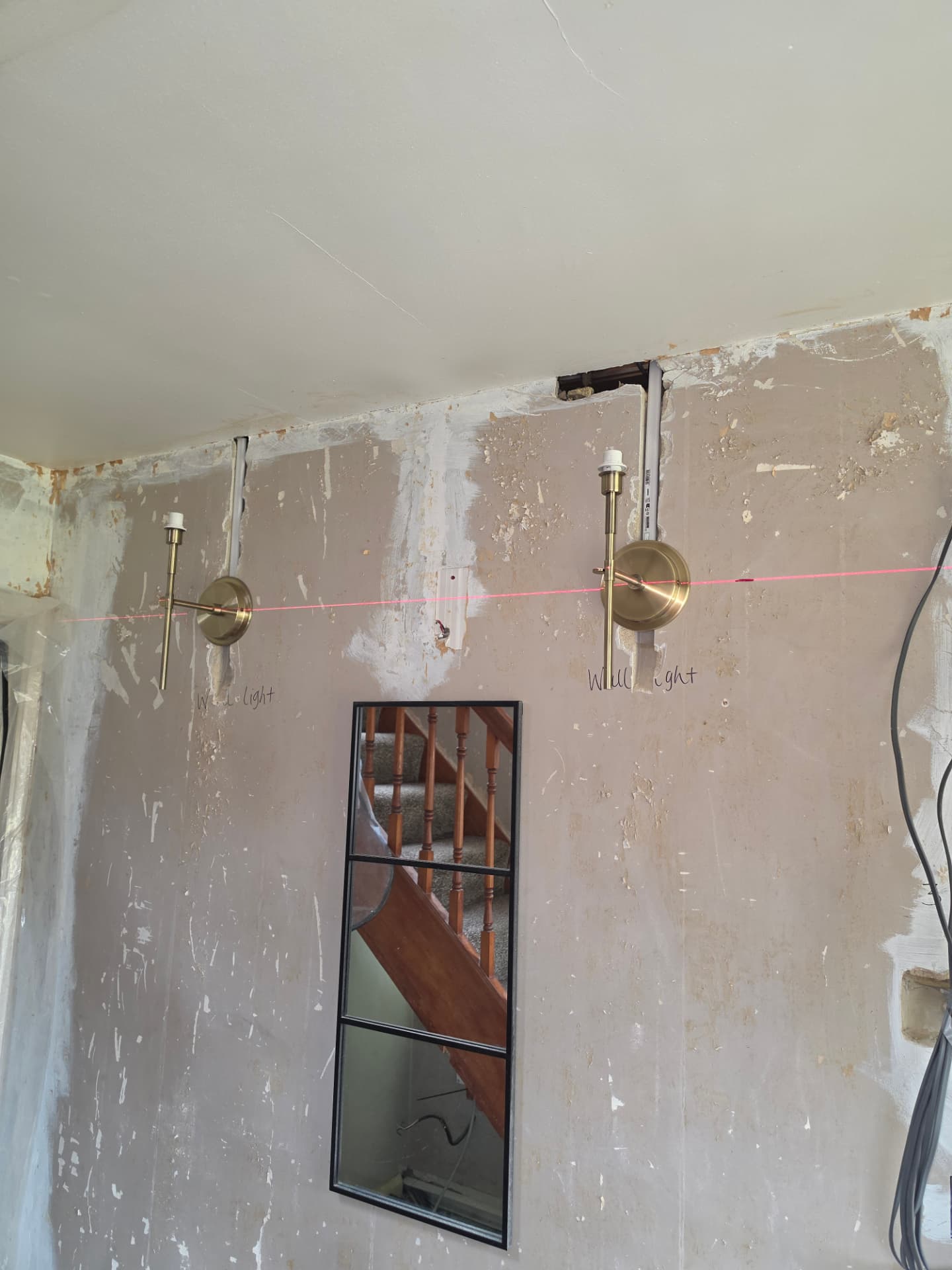 Two brass wall lights mounted on a stripped wall with a laser level line during refurbishment.
