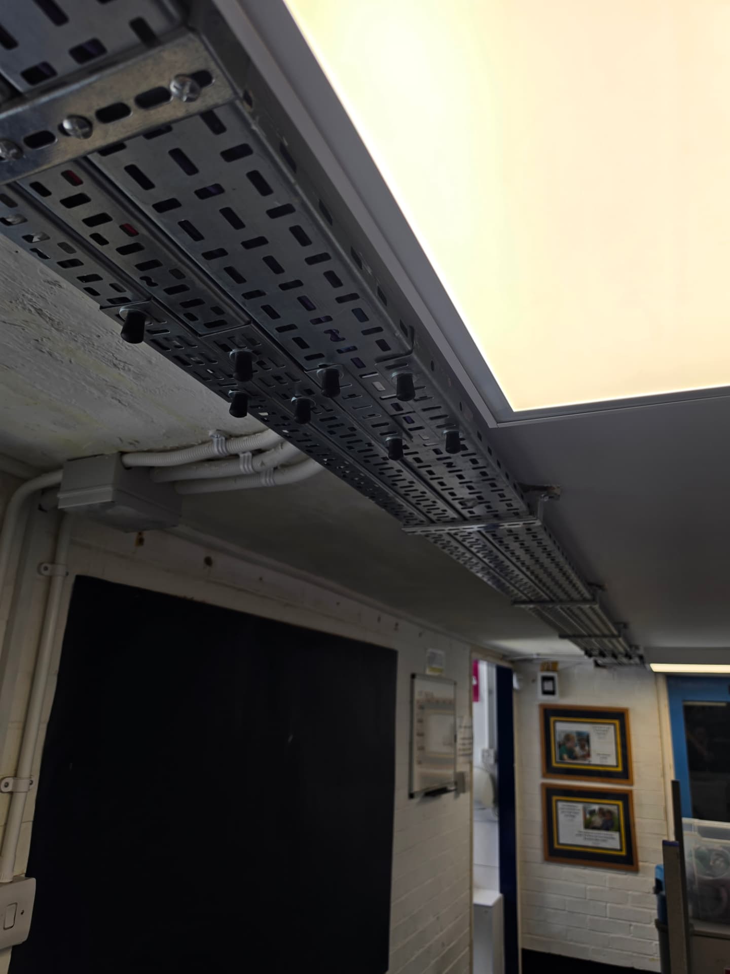 Close-up of stacked cable trays fixed alongside a ceiling light panel.
