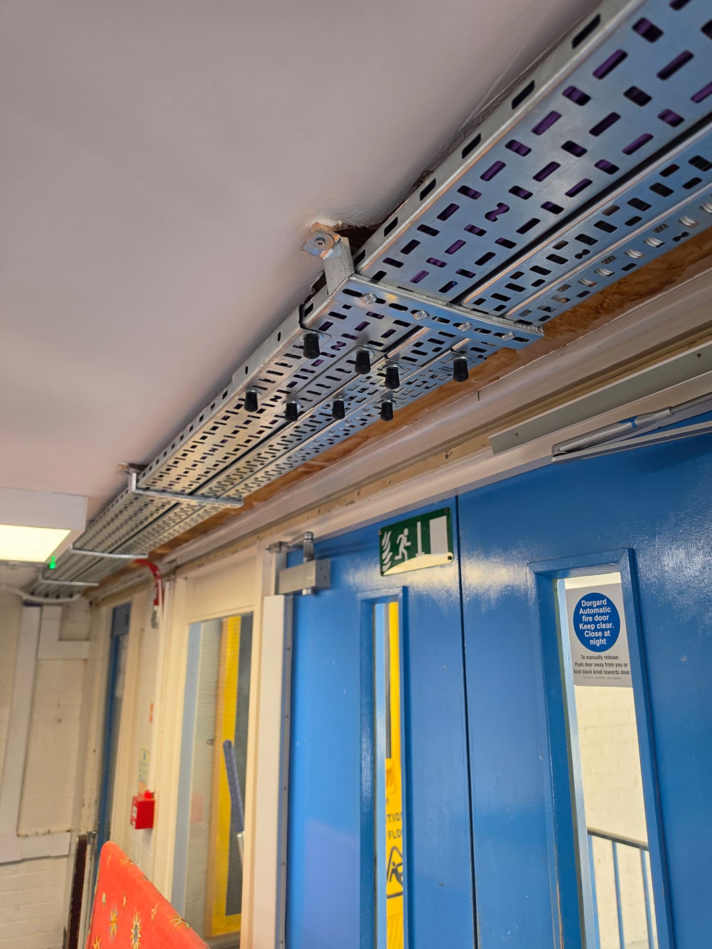 New perforated cable tray running along the corridor ceiling above a set of doors.